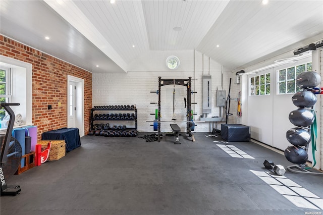 exercise room featuring electric panel, a wealth of natural light, lofted ceiling, and brick wall