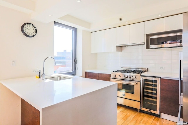 kitchen featuring appliances with stainless steel finishes, wine cooler, sink, light hardwood / wood-style flooring, and white cabinetry