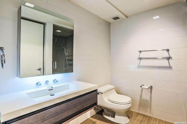 bathroom with vanity, a shower, hardwood / wood-style flooring, toilet, and tile walls