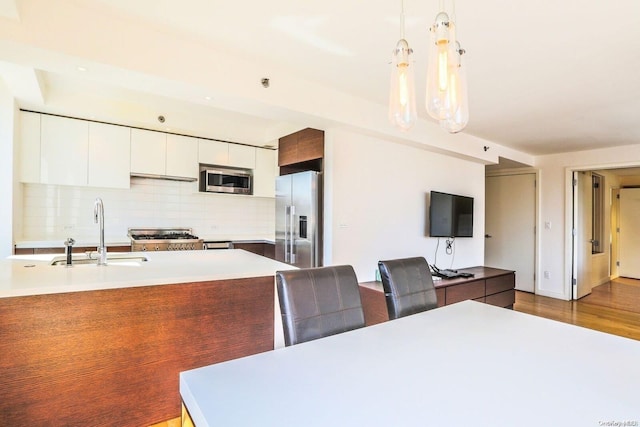 kitchen with white cabinets, sink, hanging light fixtures, appliances with stainless steel finishes, and light hardwood / wood-style floors