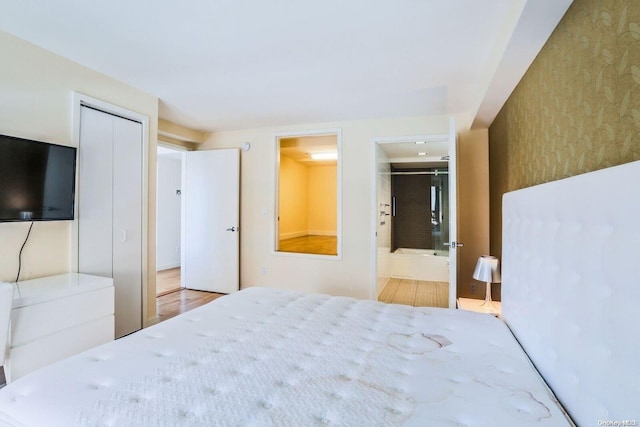 bedroom with light wood-type flooring, ensuite bathroom, and a closet