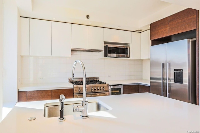 kitchen featuring beverage cooler, tasteful backsplash, white cabinetry, stainless steel appliances, and extractor fan