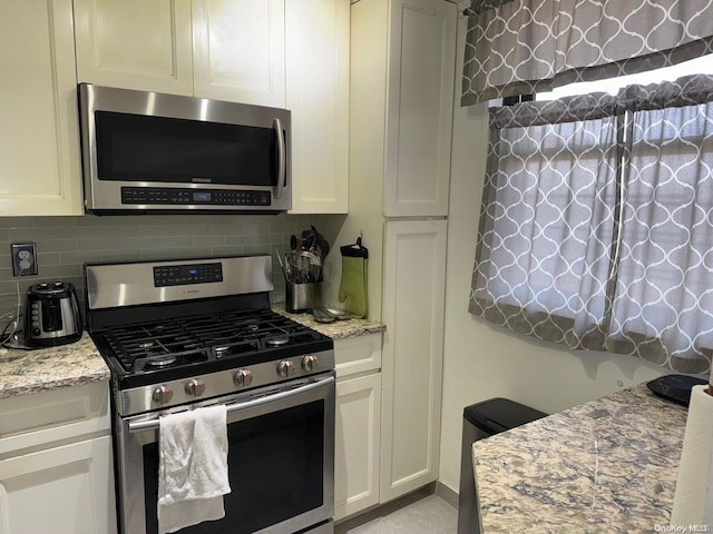 kitchen with white cabinetry, light stone countertops, stainless steel appliances, and tasteful backsplash