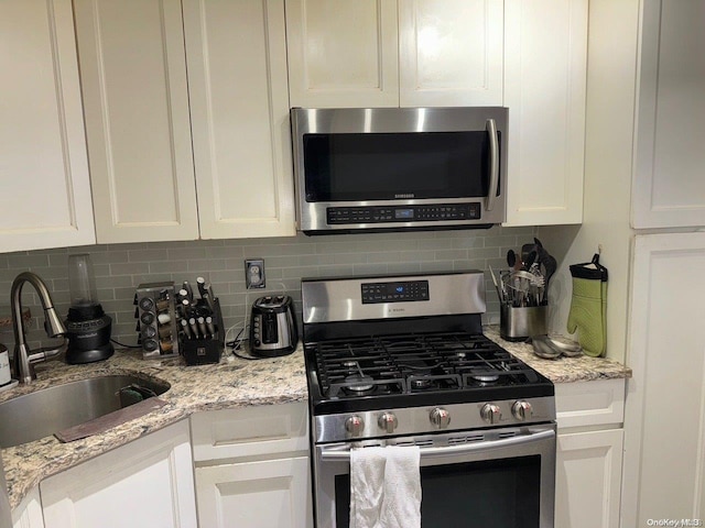 kitchen featuring light stone countertops, tasteful backsplash, stainless steel appliances, sink, and white cabinetry