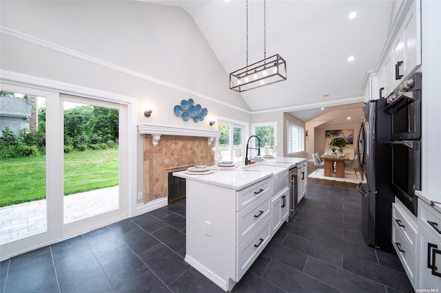 kitchen featuring white cabinetry, light stone counters, dark tile patterned floors, an island with sink, and pendant lighting