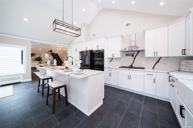 kitchen featuring stainless steel appliances, white cabinetry, wall chimney exhaust hood, and a center island with sink