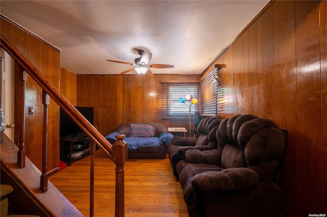 living room with light hardwood / wood-style flooring, ceiling fan, and wood walls