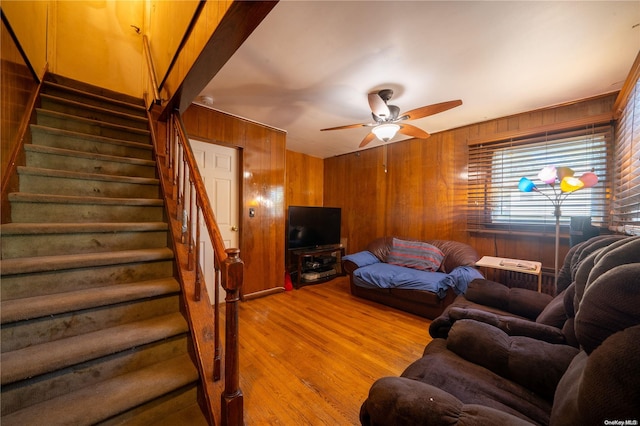 living room featuring ceiling fan, light wood-type flooring, and wooden walls