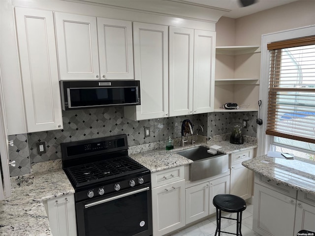 kitchen featuring decorative backsplash, gas stove, light stone countertops, and white cabinetry