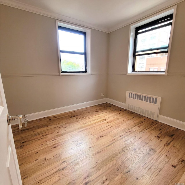 empty room with radiator heating unit, plenty of natural light, and light hardwood / wood-style flooring