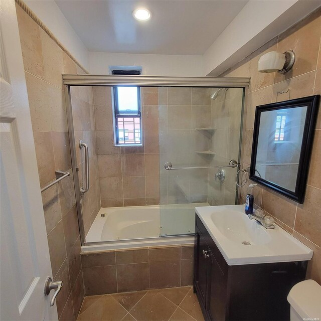 full bathroom featuring vanity, shower / bath combination with glass door, tile walls, tile patterned flooring, and toilet