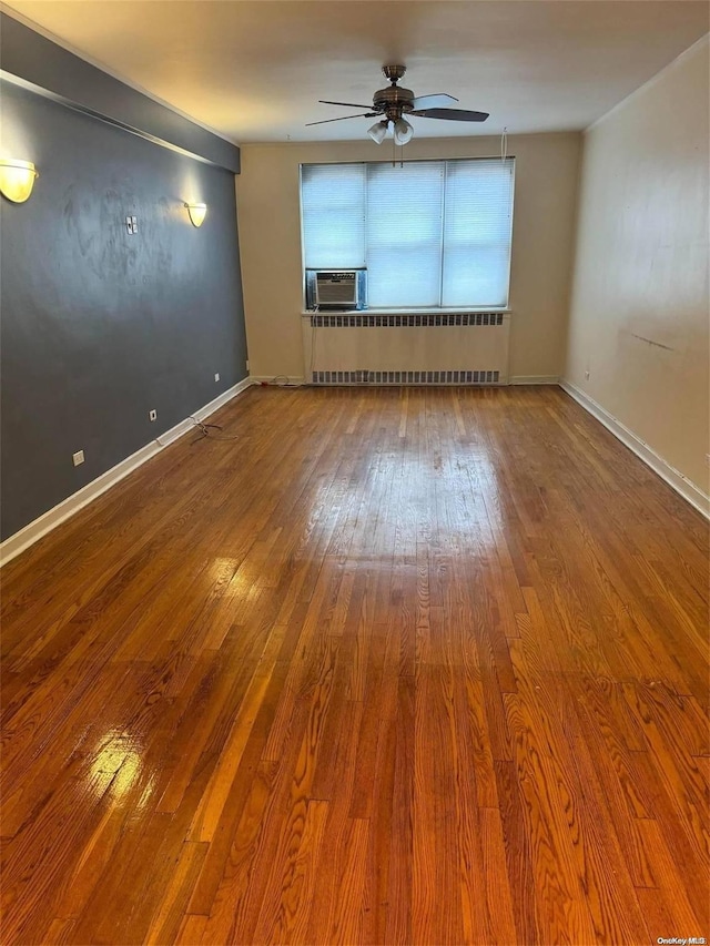 empty room featuring hardwood / wood-style flooring, ceiling fan, cooling unit, and radiator heating unit