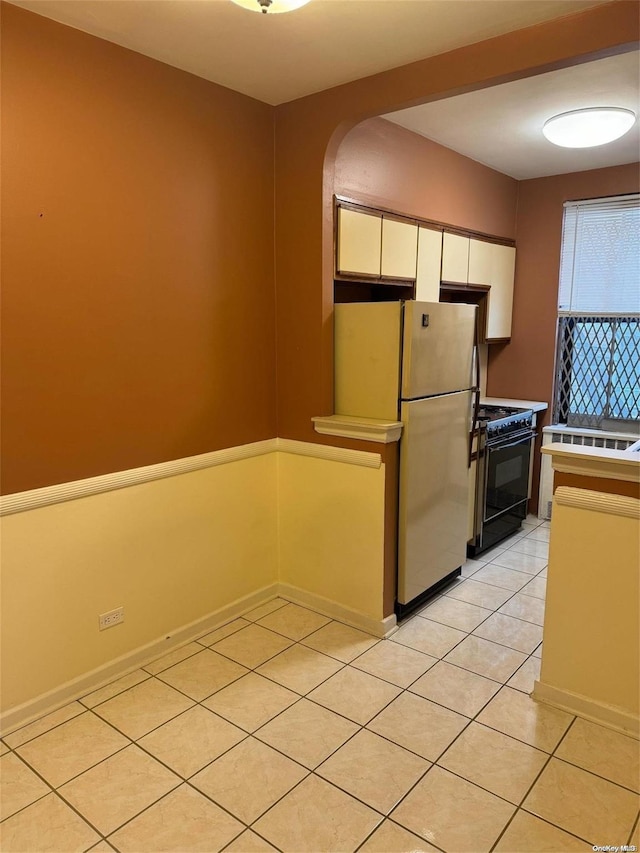 kitchen with black range with gas stovetop, white cabinets, light tile patterned flooring, and fridge