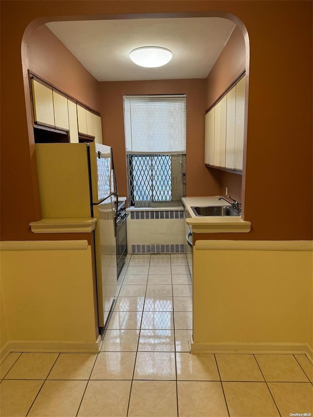 kitchen with white cabinets, light tile patterned flooring, sink, and radiator