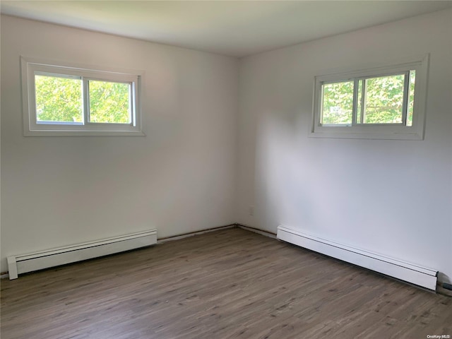 unfurnished room featuring wood-type flooring, baseboard heating, and a wealth of natural light