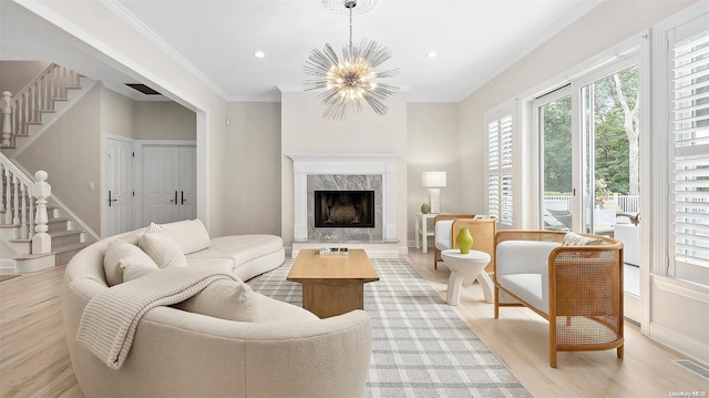 living room with light wood-type flooring, ornamental molding, a high end fireplace, and a chandelier