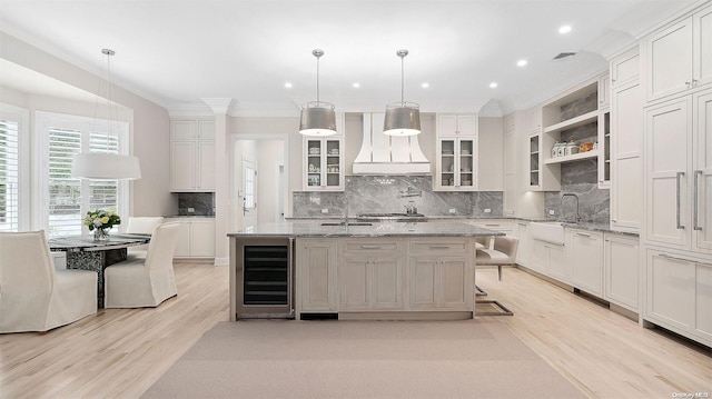 kitchen featuring pendant lighting, a kitchen island with sink, beverage cooler, and custom exhaust hood