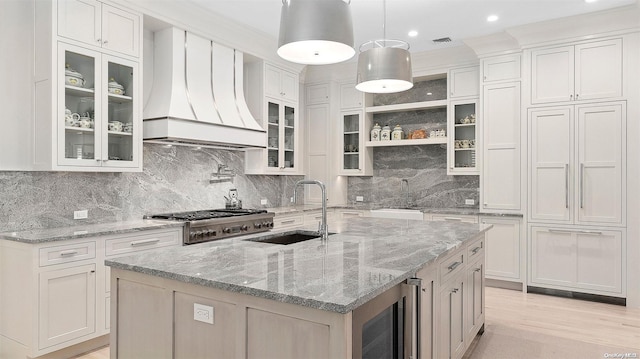 kitchen with custom exhaust hood, a kitchen island with sink, beverage cooler, sink, and white cabinetry