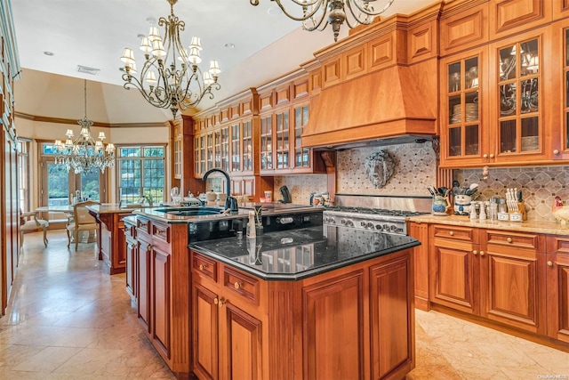 kitchen featuring backsplash, sink, pendant lighting, dark stone countertops, and an island with sink