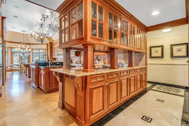 kitchen with light stone counters, a chandelier, pendant lighting, a kitchen island with sink, and ornamental molding