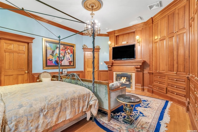 bedroom with a notable chandelier, wood walls, ornamental molding, and light hardwood / wood-style flooring