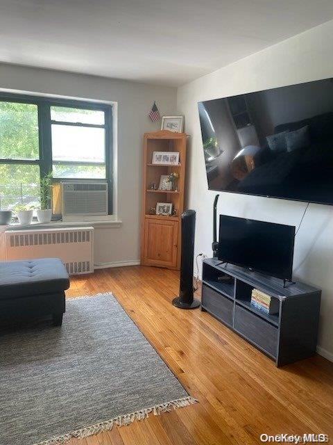 living area with radiator, wood finished floors, and cooling unit
