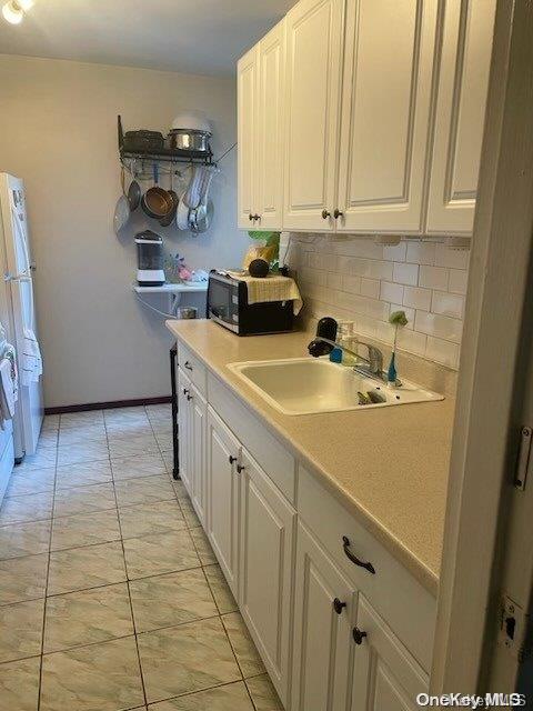 kitchen featuring backsplash, white refrigerator, white cabinetry, and sink