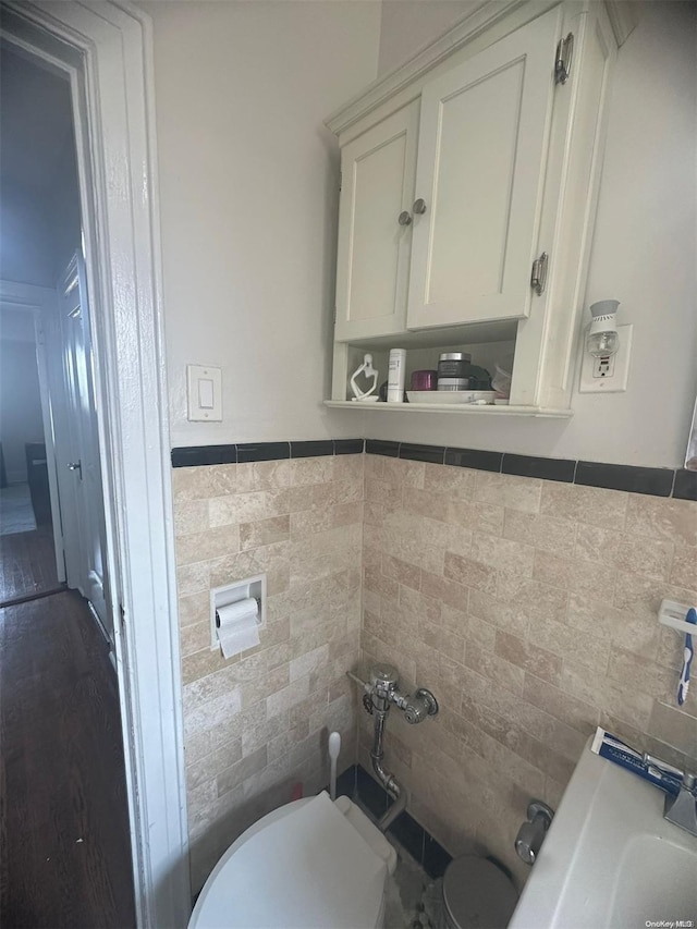 bathroom featuring wood-type flooring, toilet, and tile walls