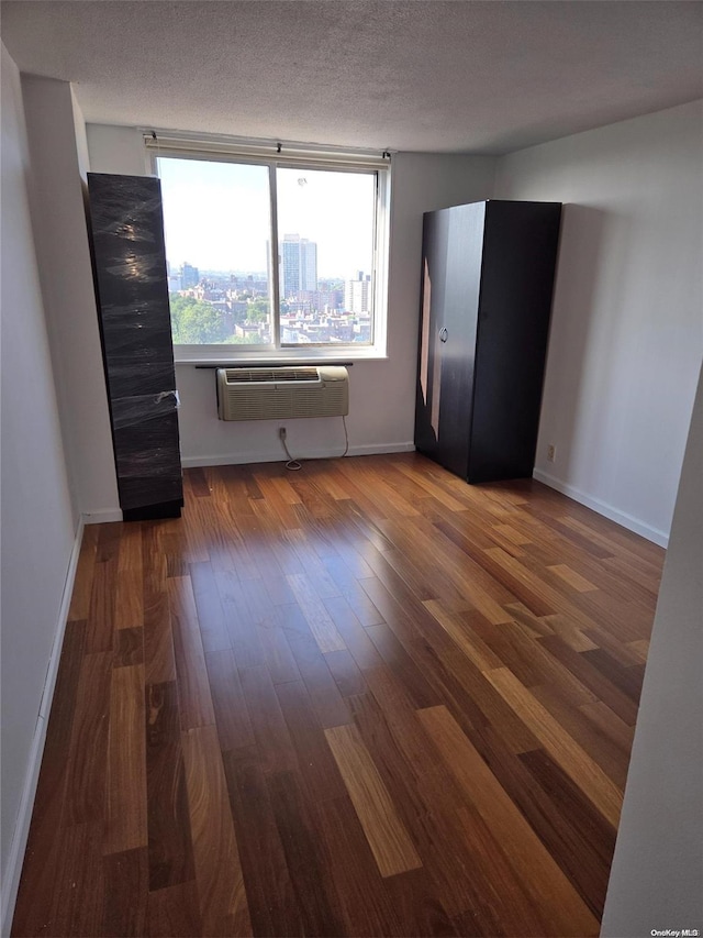 unfurnished room with a wall mounted AC, dark wood-type flooring, and a textured ceiling