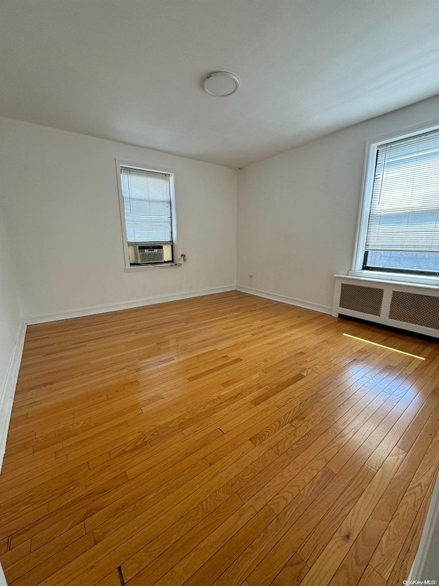 empty room with a wealth of natural light, radiator, and light hardwood / wood-style flooring