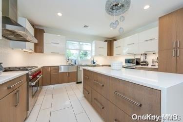 kitchen featuring appliances with stainless steel finishes, wall chimney range hood, light tile patterned floors, pendant lighting, and white cabinets