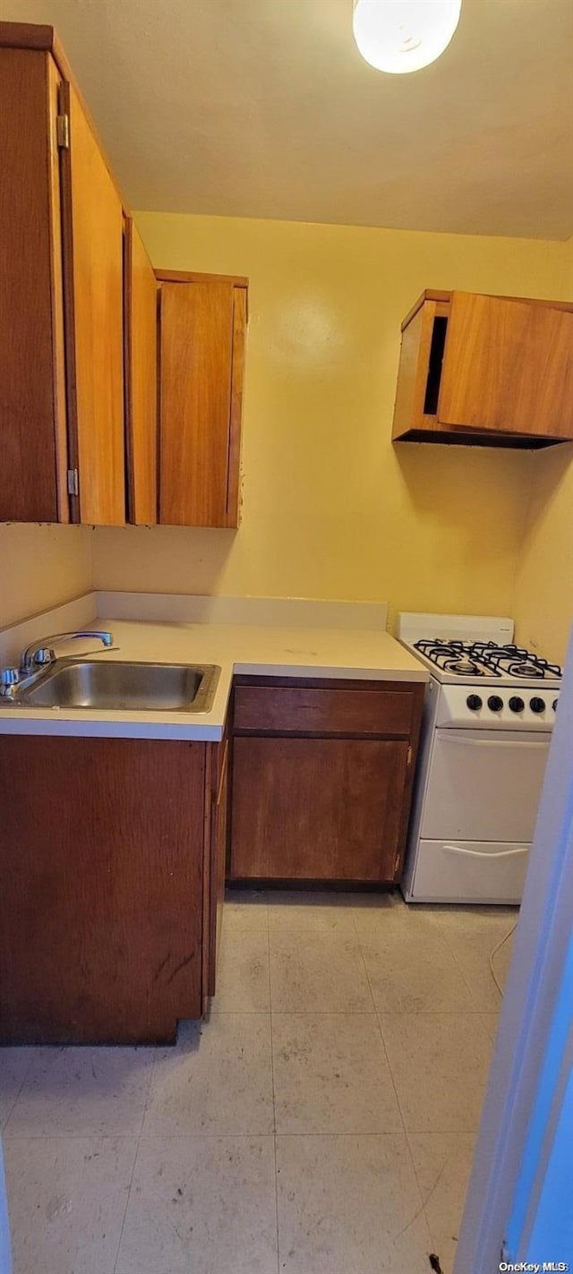 kitchen featuring white gas stove, light tile patterned floors, and sink