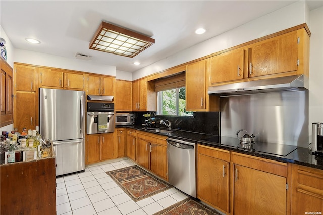 kitchen with backsplash, stainless steel appliances, sink, light tile patterned floors, and dark stone countertops