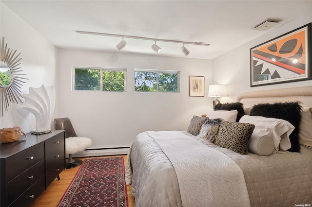 bedroom with a baseboard radiator, track lighting, and light wood-type flooring