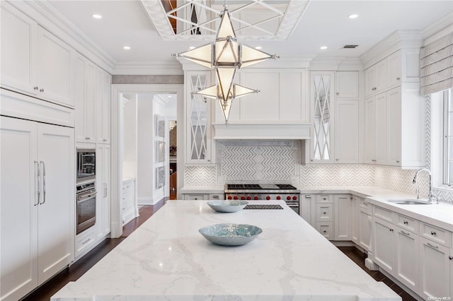 kitchen featuring light stone countertops, crown molding, sink, built in appliances, and white cabinetry