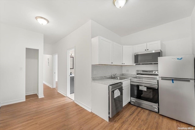 kitchen with appliances with stainless steel finishes, light hardwood / wood-style flooring, white cabinetry, and sink