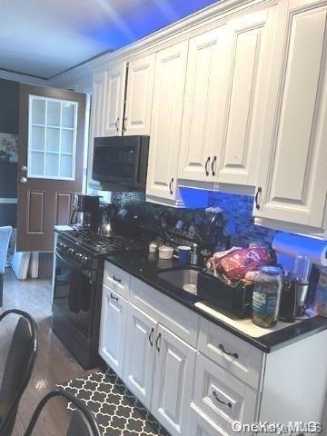 kitchen with black appliances, white cabinets, and backsplash