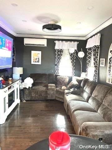 living room with an AC wall unit, crown molding, and dark wood-type flooring