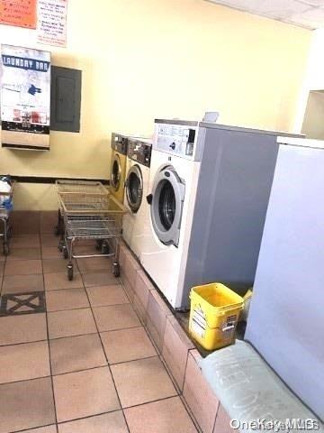 clothes washing area featuring light tile patterned floors, electric panel, and washer and clothes dryer