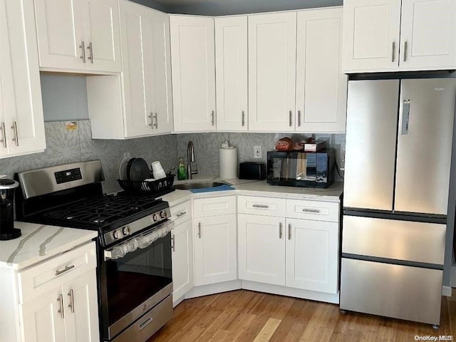 kitchen featuring backsplash, white cabinets, sink, light hardwood / wood-style flooring, and appliances with stainless steel finishes