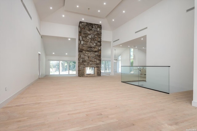 unfurnished living room with a stone fireplace, light wood-type flooring, and a high ceiling