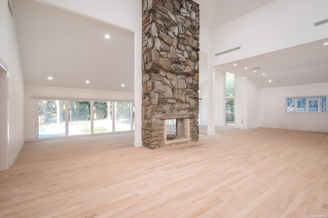 unfurnished living room featuring light wood-type flooring, high vaulted ceiling, and a stone fireplace