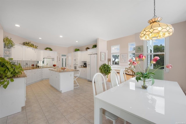 kitchen featuring pendant lighting, a center island, white appliances, white cabinets, and light tile patterned flooring