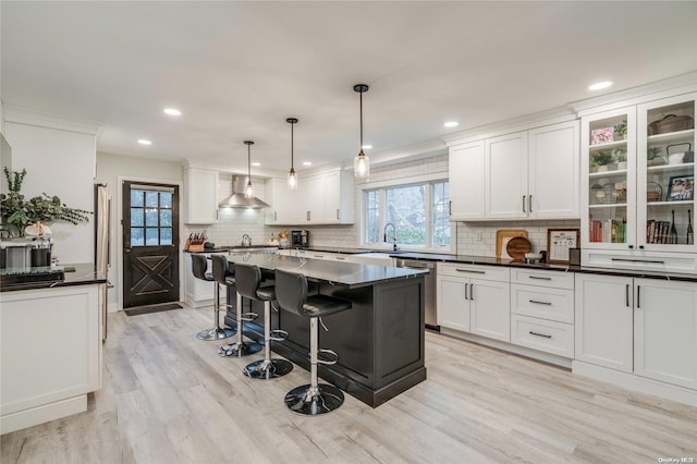 kitchen with a center island, white cabinets, wall chimney range hood, light hardwood / wood-style flooring, and decorative light fixtures