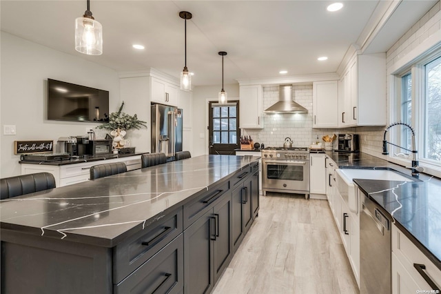 kitchen with pendant lighting, stainless steel appliances, white cabinetry, and wall chimney exhaust hood