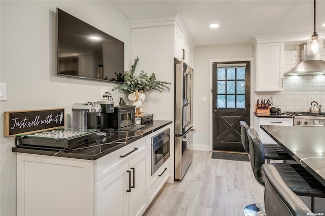 kitchen featuring white cabinets, decorative light fixtures, wall chimney range hood, and stainless steel appliances