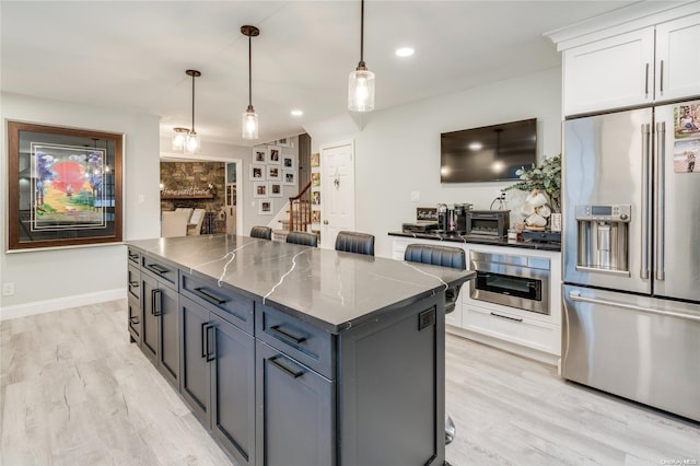 kitchen featuring white cabinetry, pendant lighting, stainless steel appliances, and light wood-type flooring