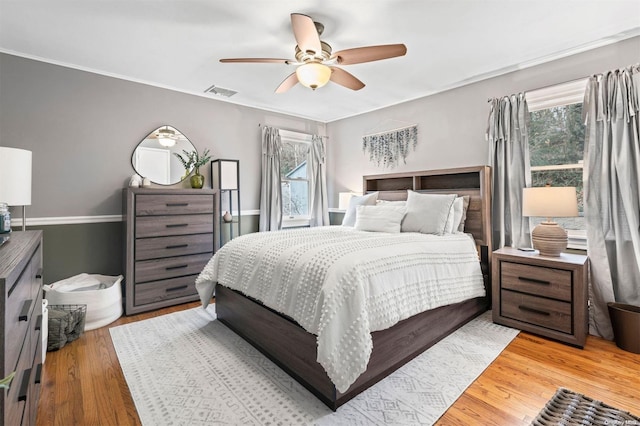 bedroom featuring multiple windows, ceiling fan, wood-type flooring, and ornamental molding