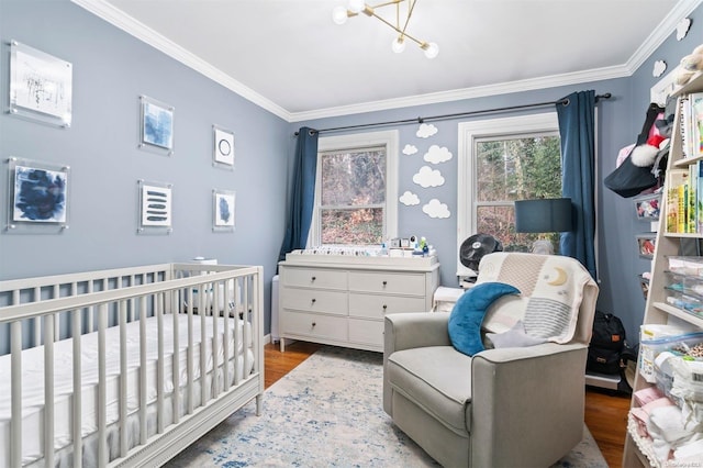 bedroom featuring a crib, light wood-type flooring, crown molding, and a notable chandelier