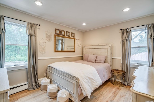 bedroom featuring baseboard heating, light hardwood / wood-style flooring, and multiple windows